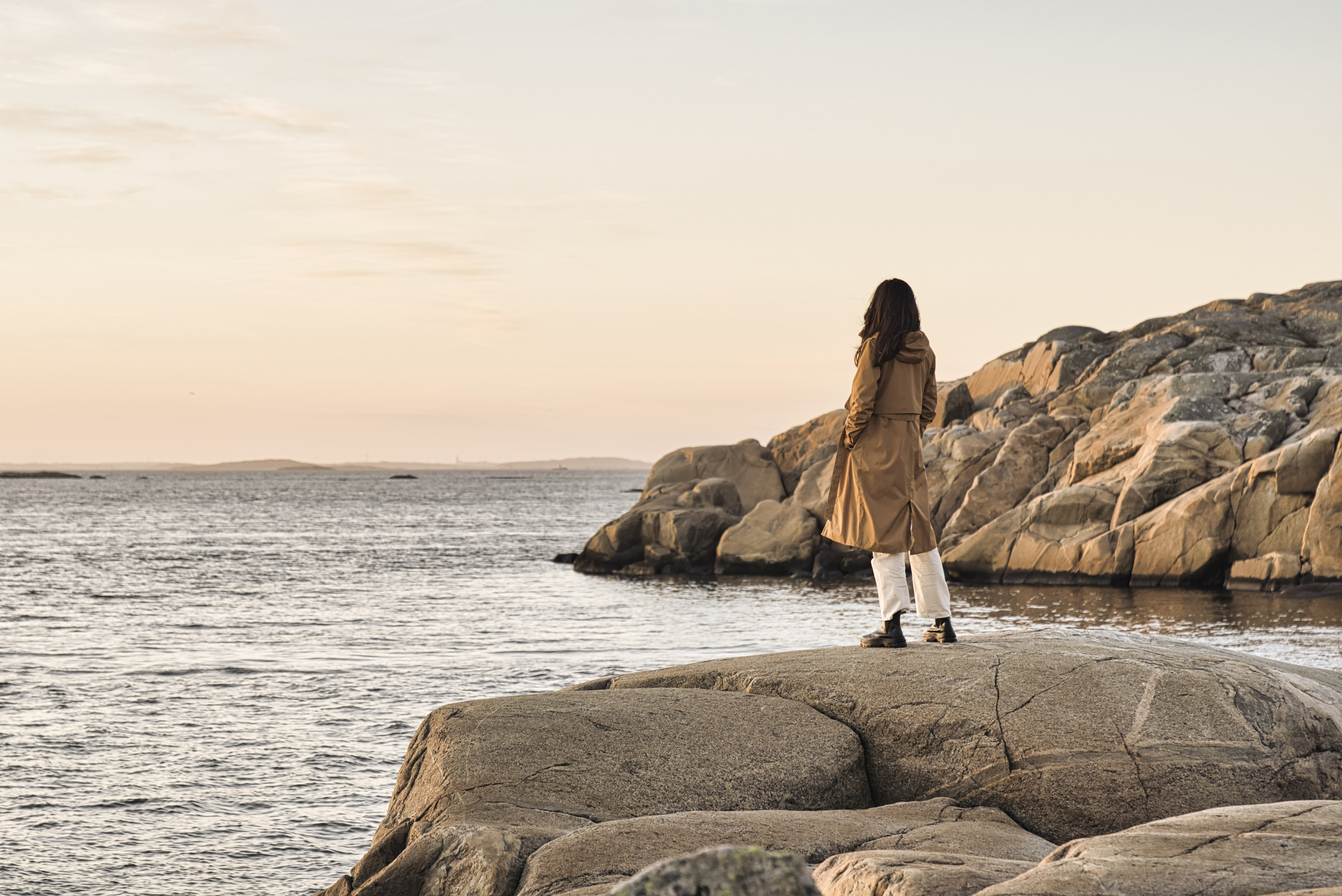 Woman standing on rocks by the sea looking at the sunset