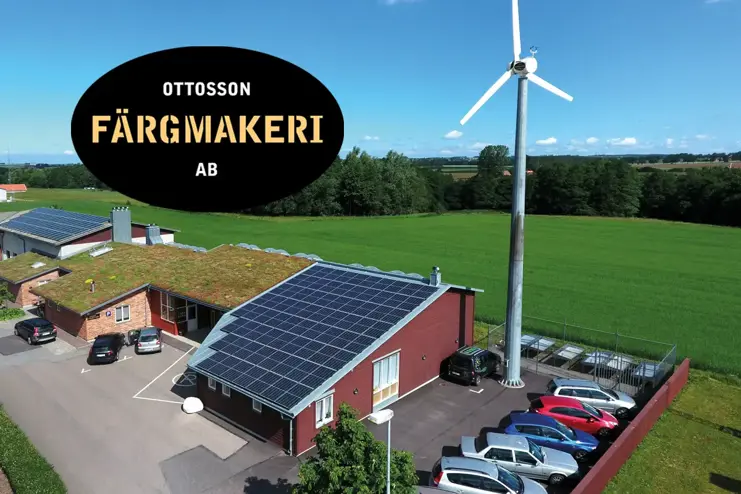 Aerial view of Ottosson Färgmakeri facility featuring solar panels, a wind turbine, and green fields, with logo in top left.