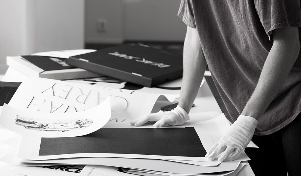 Person wearing white gloves handling art prints and exclusive books on a table