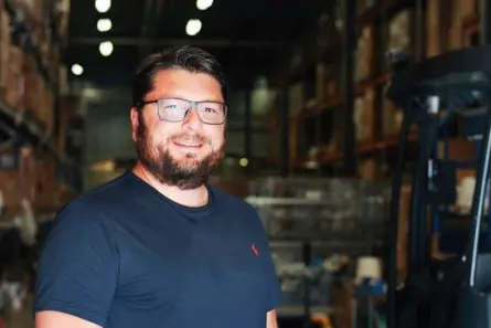 Smiling man with glasses in a warehouse with shelving and forklift