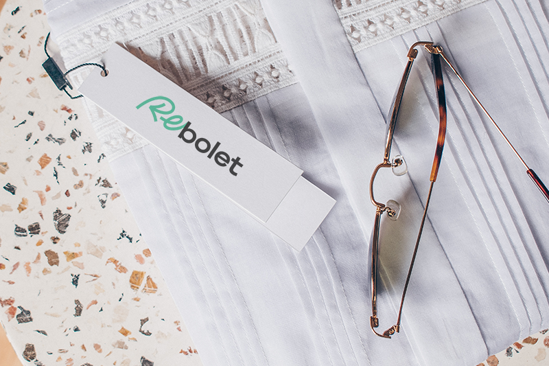 Rebolet clothing tag on white fabric with glasses next to it