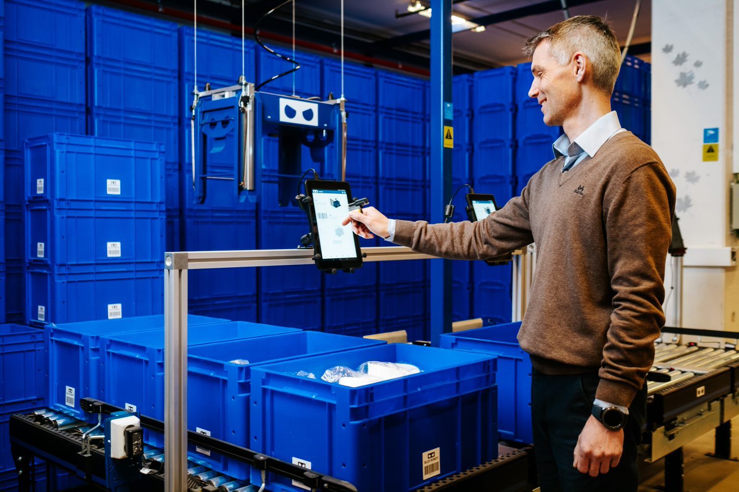 Man using tablet to operate picking station in an automated warehouse with blue bins.