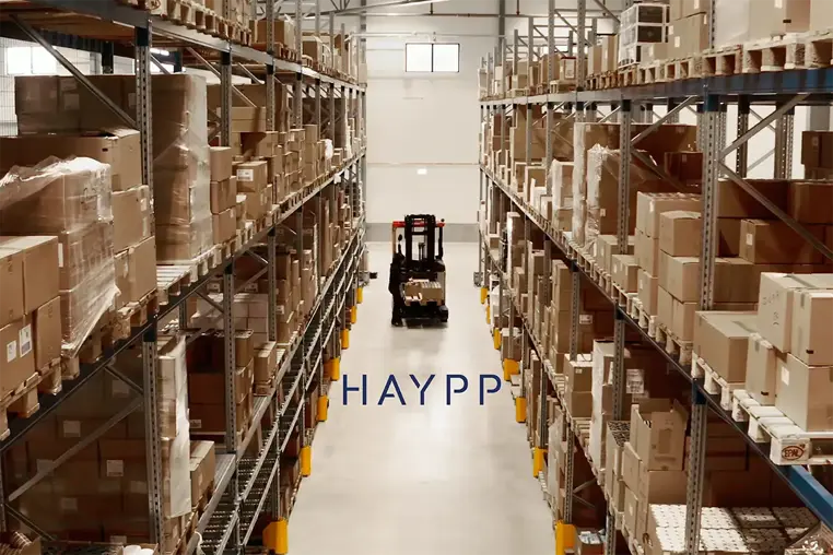 High warehouse aisle filled with stacked box shelves, a forklift in the distance, and the Haypp logo centered.