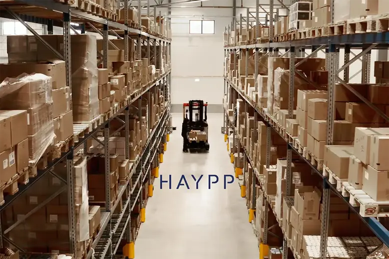Hög lagergång fylld med kartonger på hyllor, en gaffeltruck i bakgrunden och Haypp-logotypen i mitten.